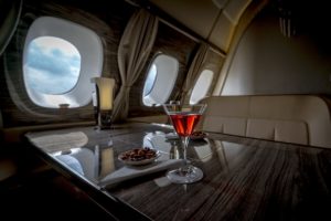 Interior of a business class of a commercial passenger plane, an armchair and a window, a table and a cocktail glass with a drink and almonds. Focus on a glass.